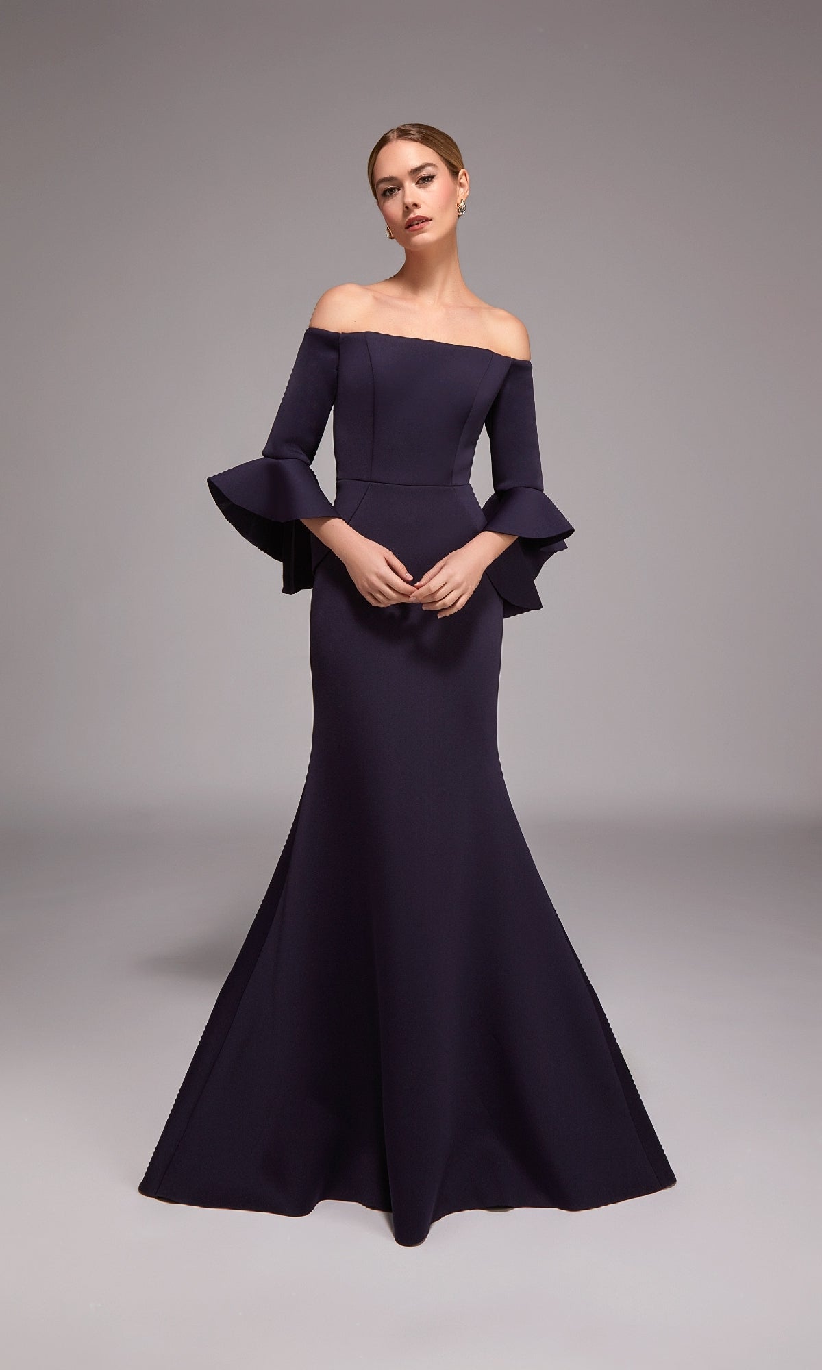 A woman models the Alyce 27777 long formal dress in navy, featuring an off-the-shoulder mermaid design with flared sleeves, against a plain gray background.